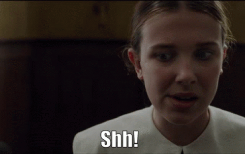 Gif com a Enola Holmes, no qual sinaliza silêncio através da expressão "Shh!"